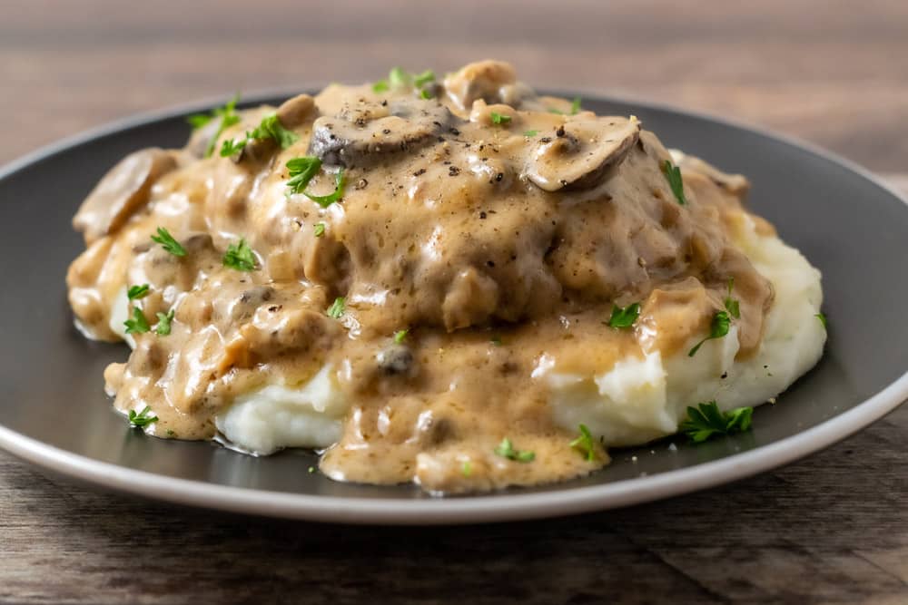 Burger Steak with Mushroom Gravy over mashed potatoes on a plate.