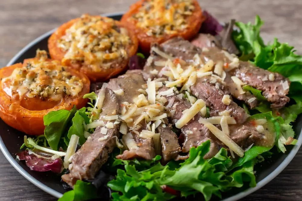 salad greens topped with steak, parmesan cheese, and dressing with 3 parm broiled tomatoes