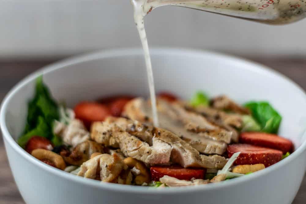 Best Poppy Seed Dressing pouring over Strawberry Chicken Salad.