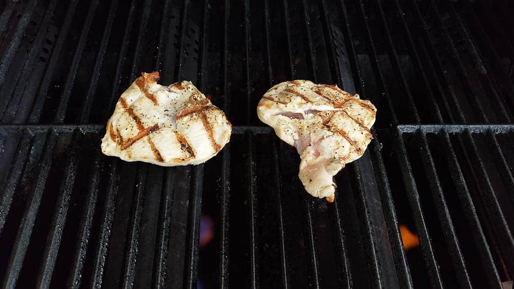 two chicken filets cooking on a grill.