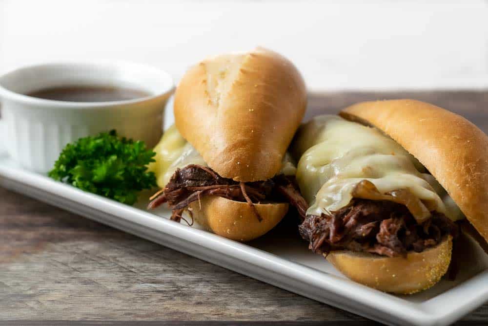 Two slow cooker crock pot French Dip Sandwiches with Au Jus sauce.