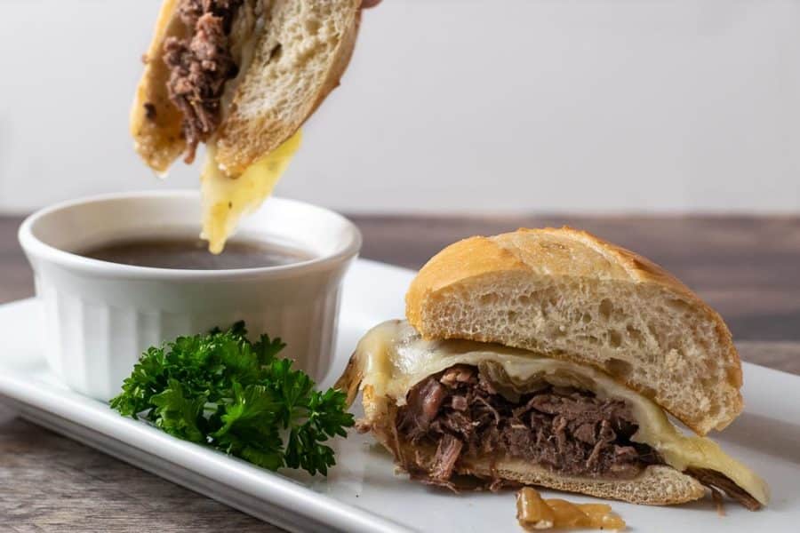 Crockpot French Dip Sandwich dipping into Au Jus