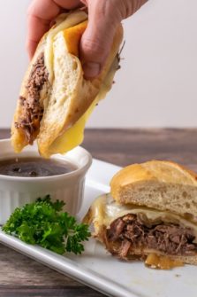 Crockpot French Dip Sandwich being dipped into au jus sauce.