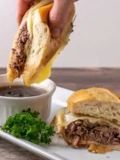 Crockpot French Dip Sandwich being dipped into au jus sauce.