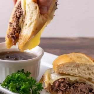 Crockpot French Dip Sandwich being dipped into au jus sauce.