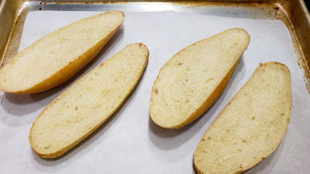 two hoagie sandwich rolls split on a baking sheet.