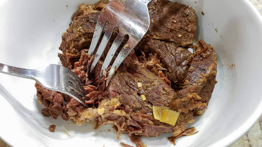 two forks shredding cooked beef roast.