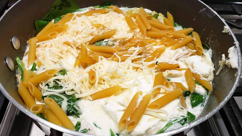 cheese, pasta, spinach, chicken and cream sauce cooking in a pan