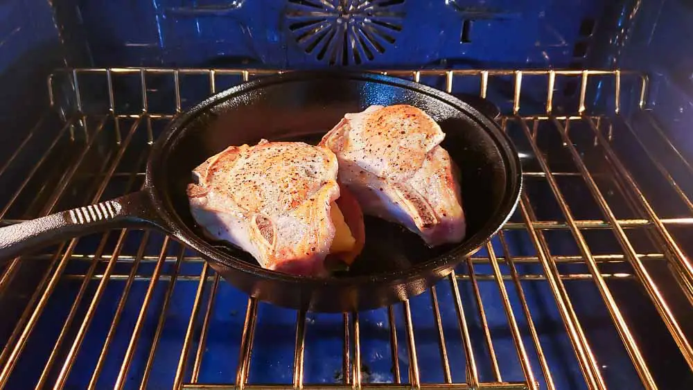 a cast iron skillet with two stuffed pork chops placed in an oven.