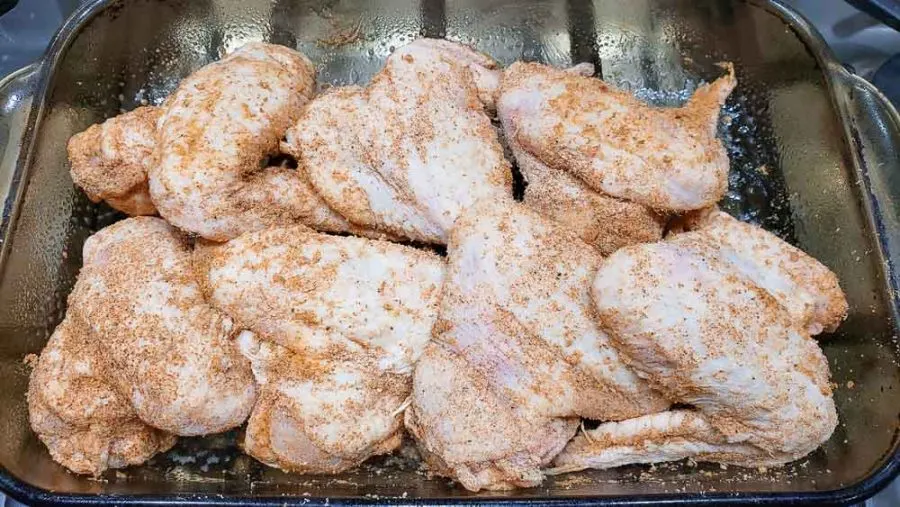 raw chicken wings sprinkled with seasonings in a baking dish.