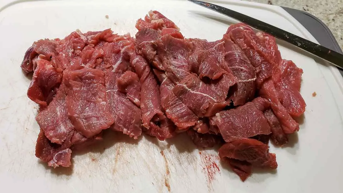 thin sliced beef on a cutting board with a knife.
