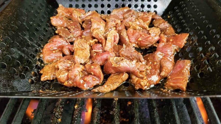 korean bbq beef slices grilling in a grill basket