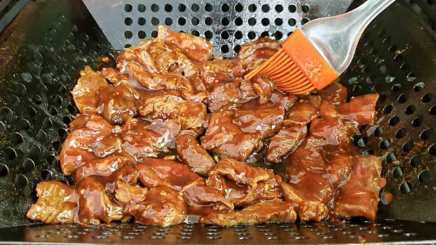 a brush slathering more korean bbq sauce onto steak slices in a grill basket