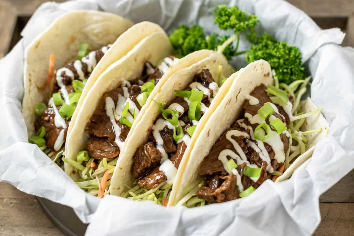 four easy Korean beef BBQ Tacos with broccoli slaw in a paper lined basket with parsley.