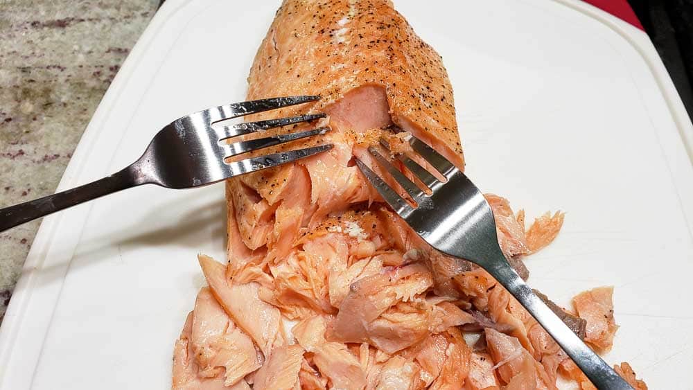 two forks flaking cooked salmon.
