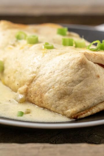 a crispy chicken chimi topped with white sauce and green onions.