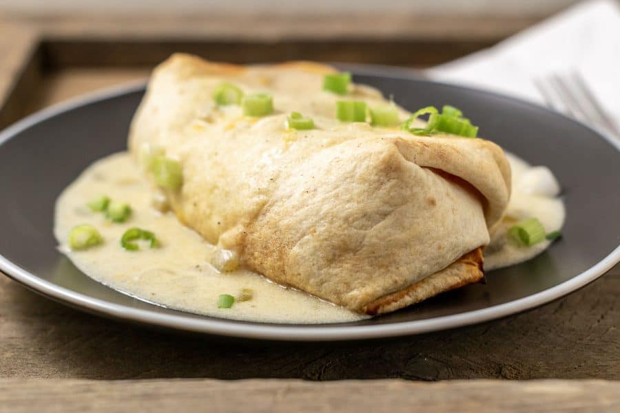 a baked chimichanga covered in green chile sauce on a plate