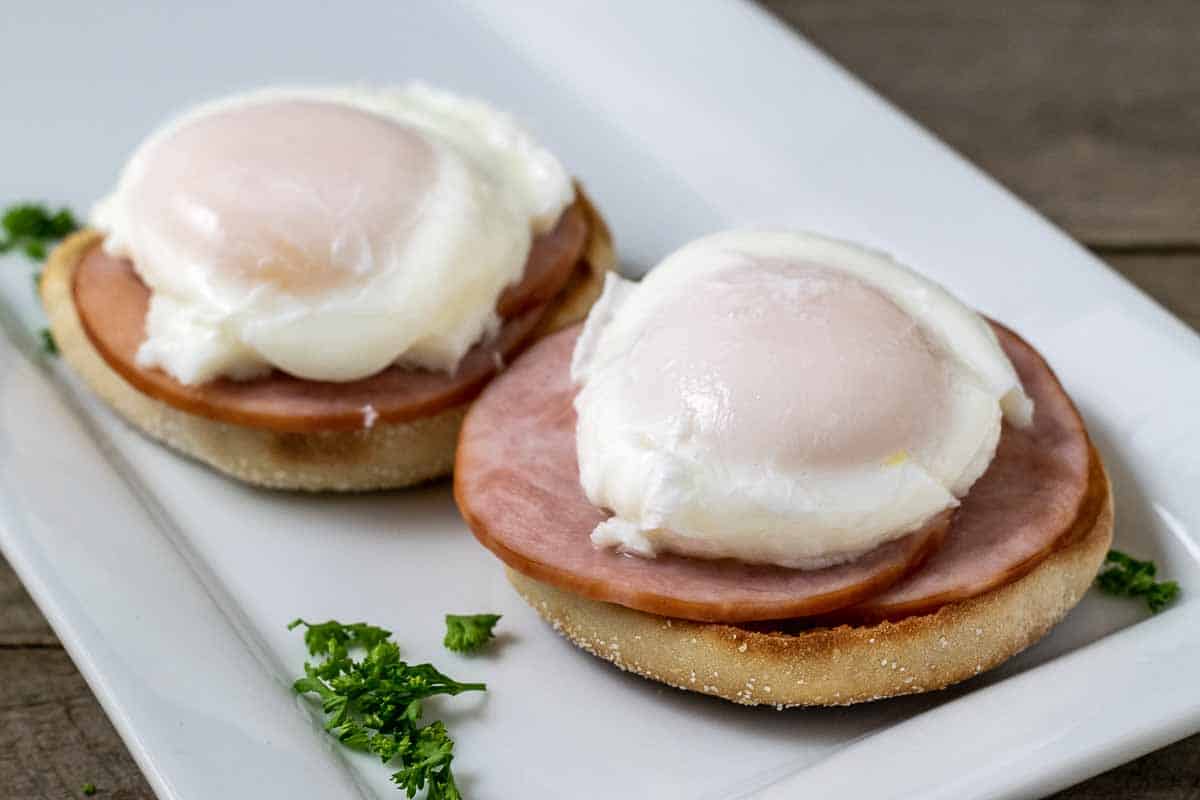english muffin halves topped with canadian bacon and poached eggs on a platter.