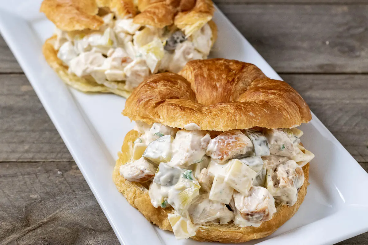 two swiss cheese and dill pickle chicken salad croissant sandwiches on a platter.