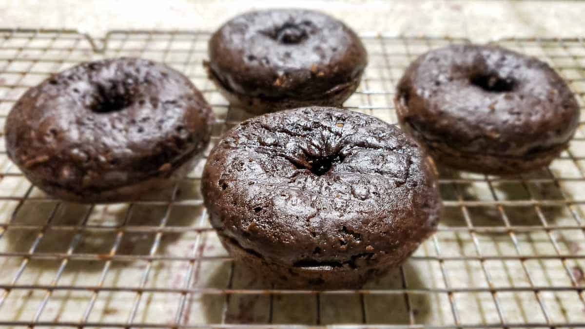 4 baked chocolate donuts cooling on a rack