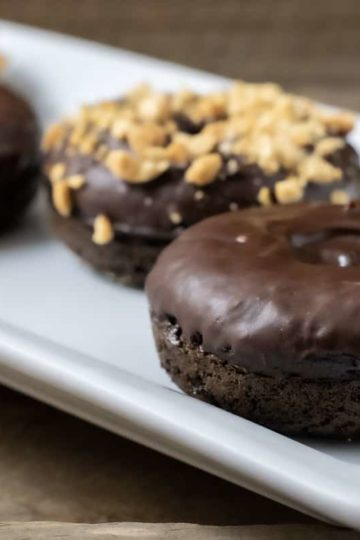 4 Baked Chocolate Donuts with Chocolate Glaze on a plate and two have nuts on top