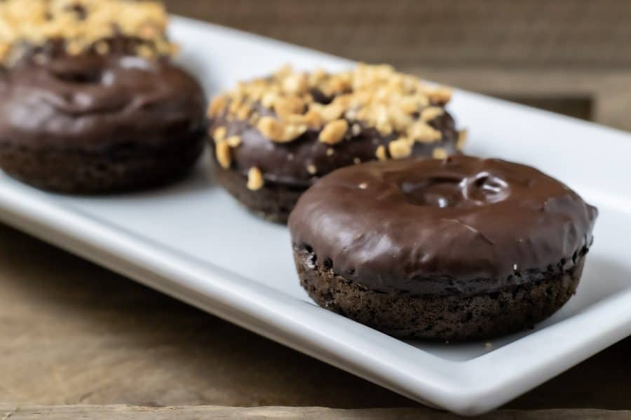 4 Baked Chocolate Donuts with Chocolate Glaze on a plate and two have nuts on top