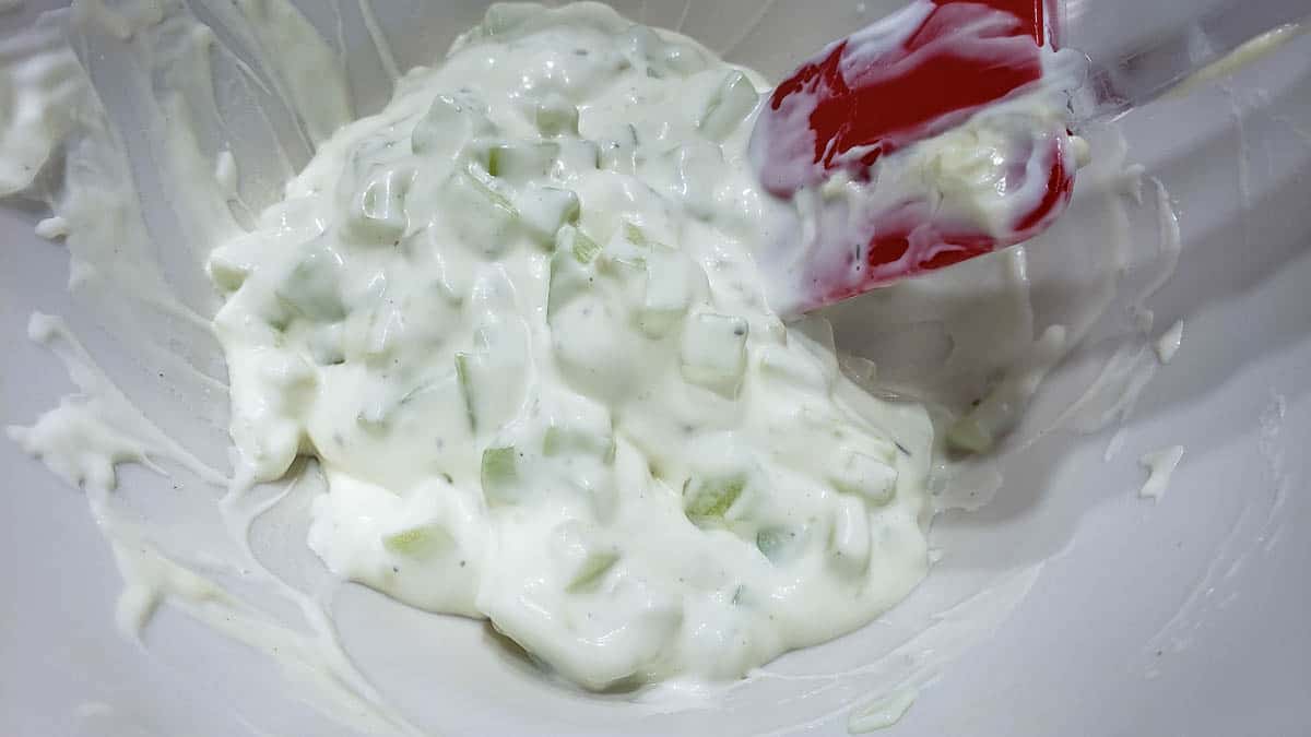sour cream, mayo, ranch salad dressing, and diced cucumber mixed in a bowl.