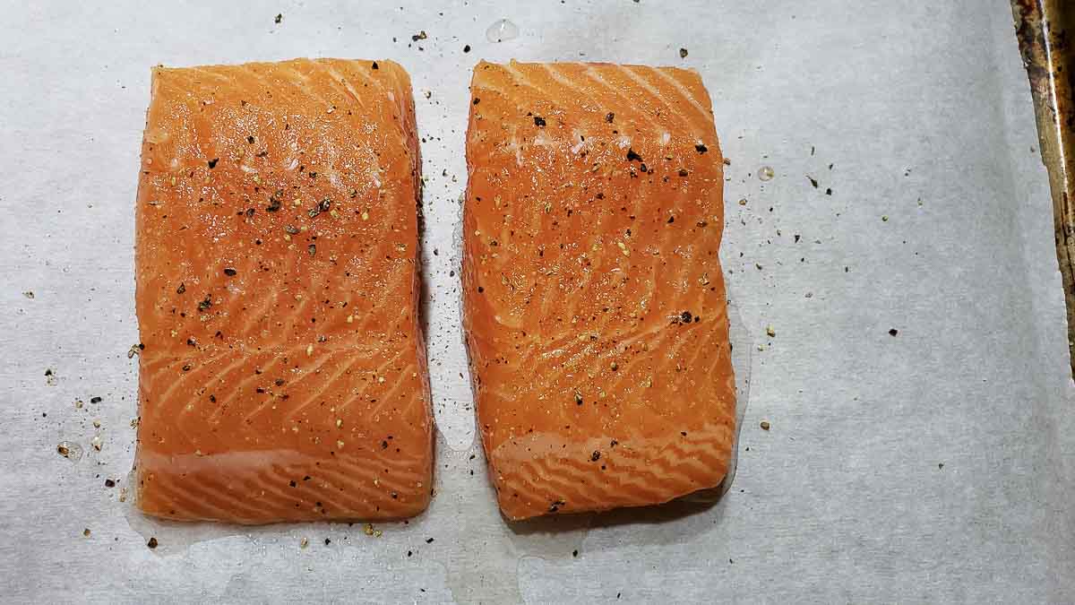 raw salmon filet sprinkled with salt and pepper on a baking tray.