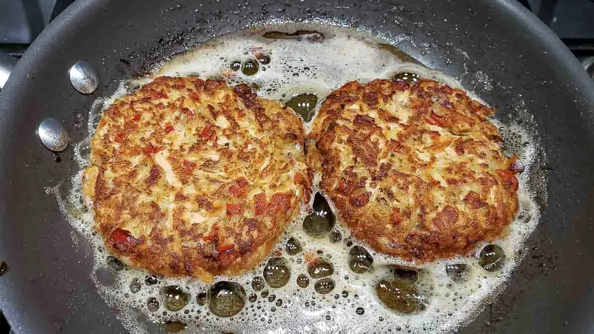two from scratch salmon burger patties frying in a pan.