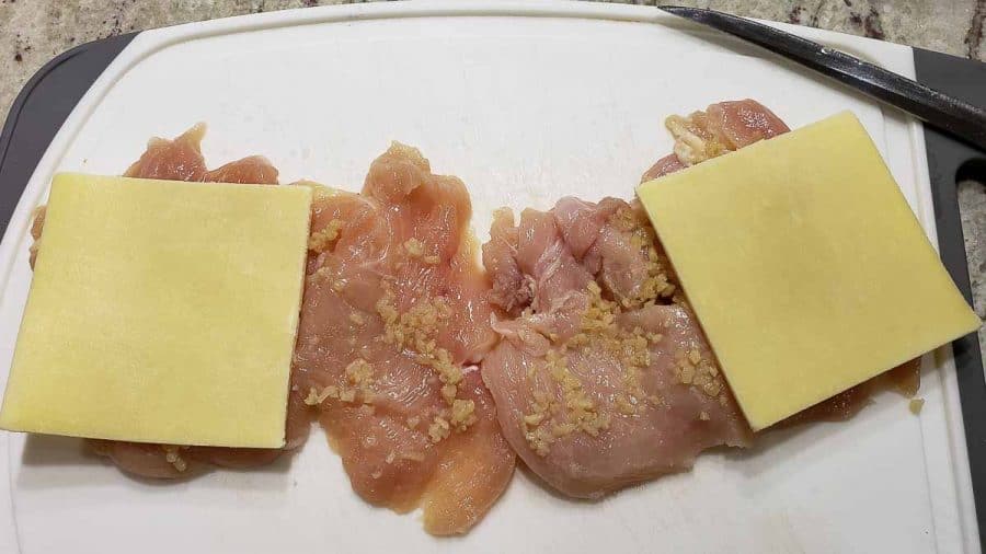 white cheddar slices layered over garlic on two chicken filets