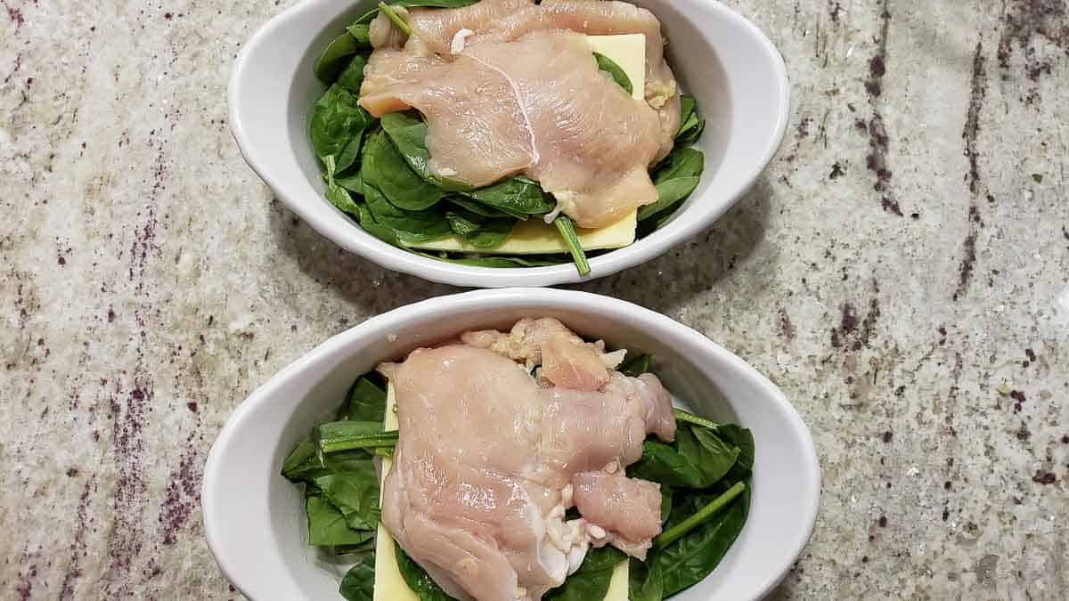 two baking dishes with chicken, spinach, and cheese.