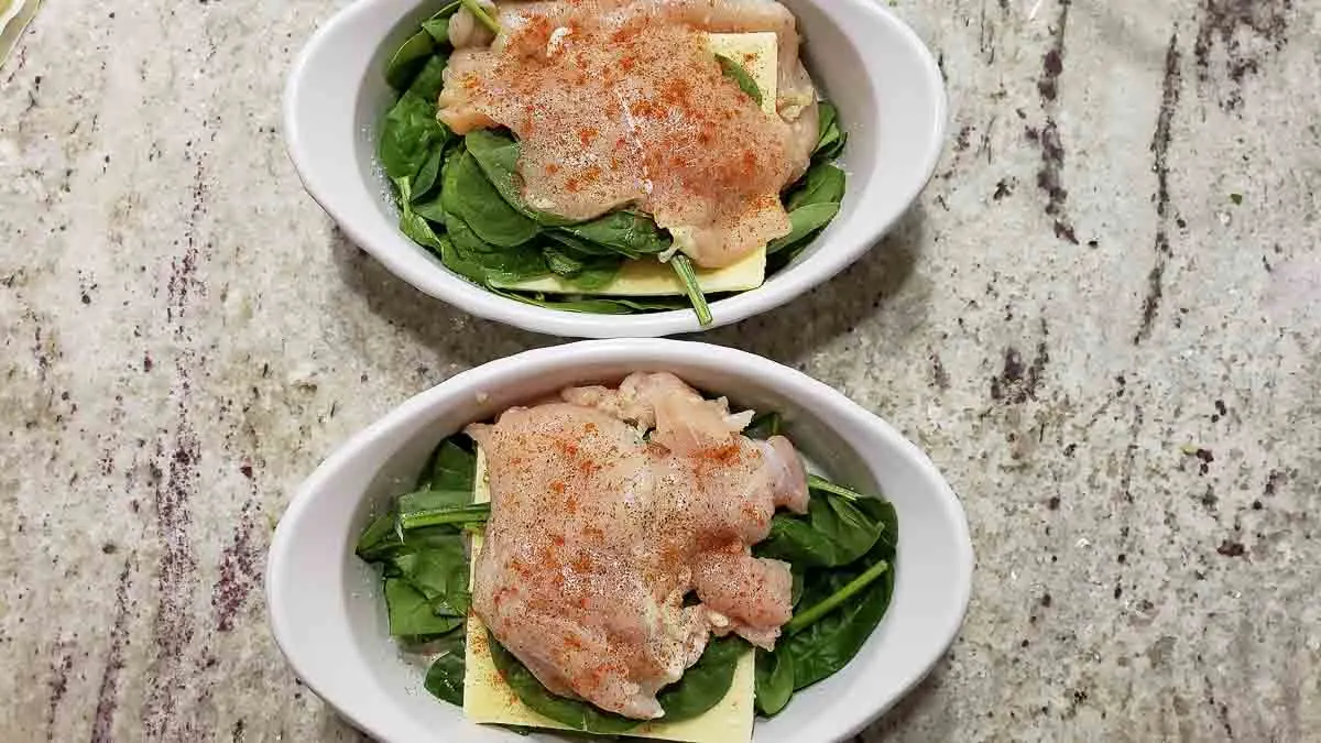 paprika sprinkled on top of cheesy spinach stuffed chicken in two baking dishes.
