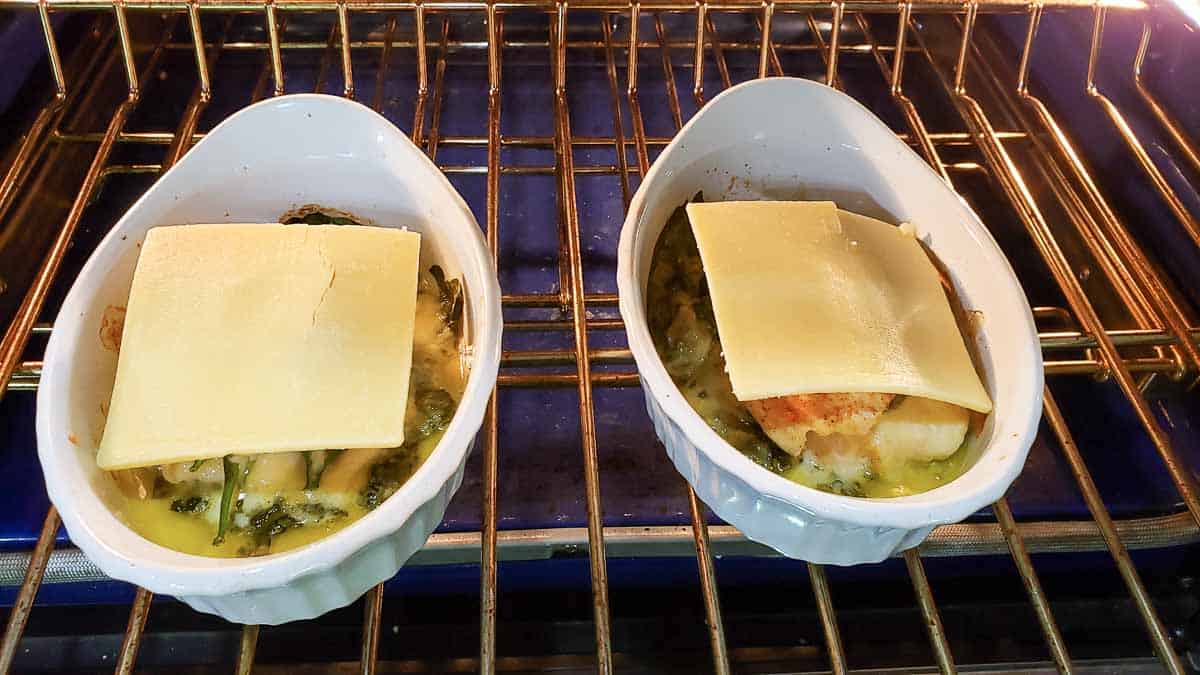 white cheddar slices added to top of baked stuffed chicken in two dishes inside oven.