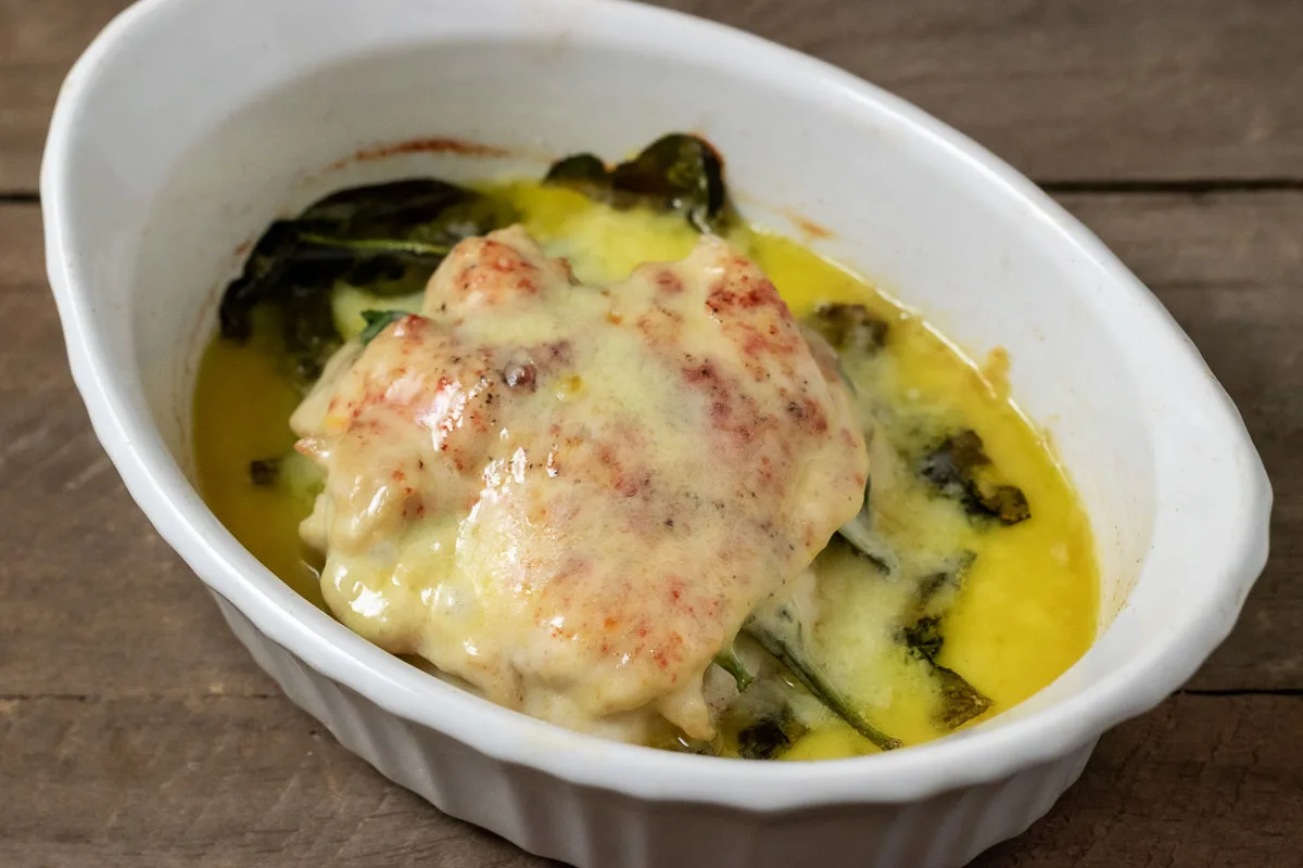 Top down view of Cheesy Spinach Stuffed Chicken in a baking dish with melted white cheddar.