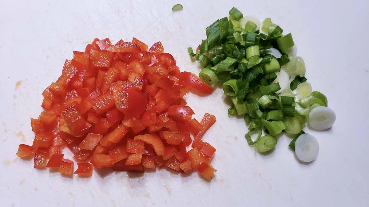 diced green onion and diced red pepper on a cutting board.