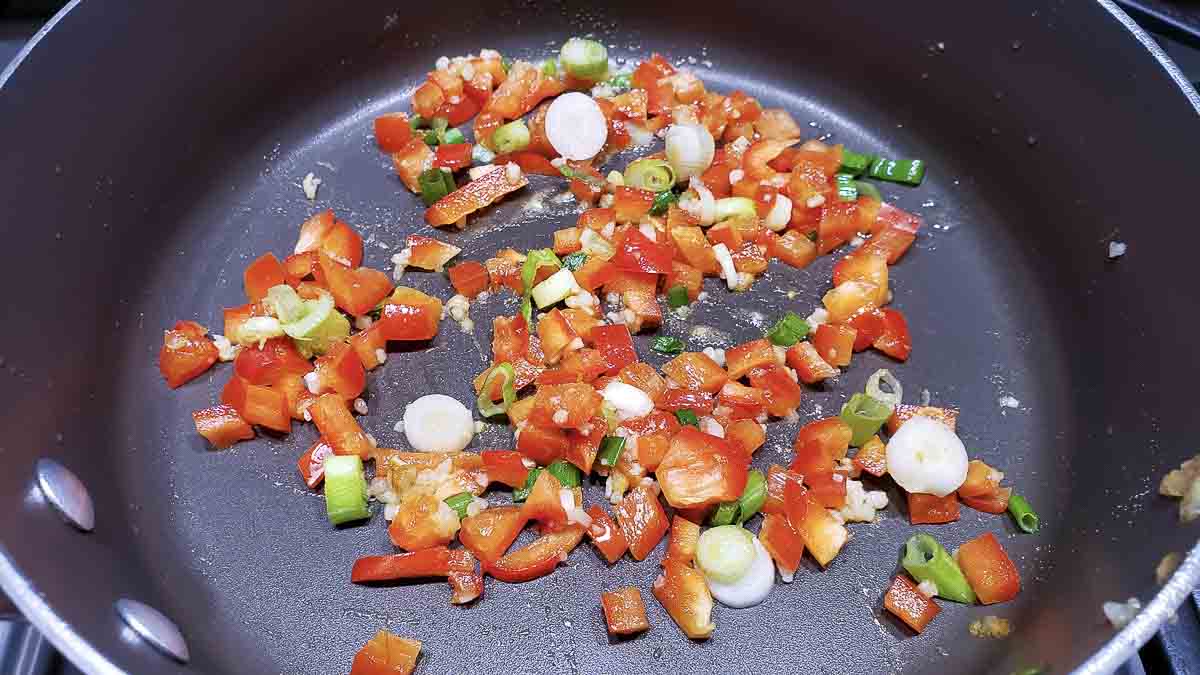 green onion, red pepper, garlic, and ginger cooking in a pan.
