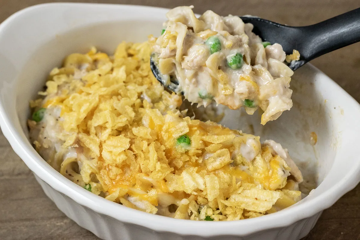 Classic Tuna Noodle Casserole with Cheese and potato chips in a baking dish with a spoon lifting out some casserole.