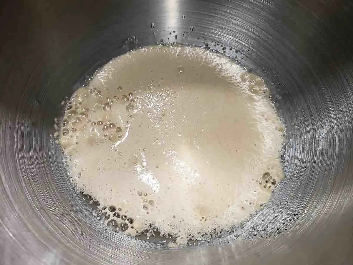 yeast, sugar, and warm water activiating in a silver bowl.