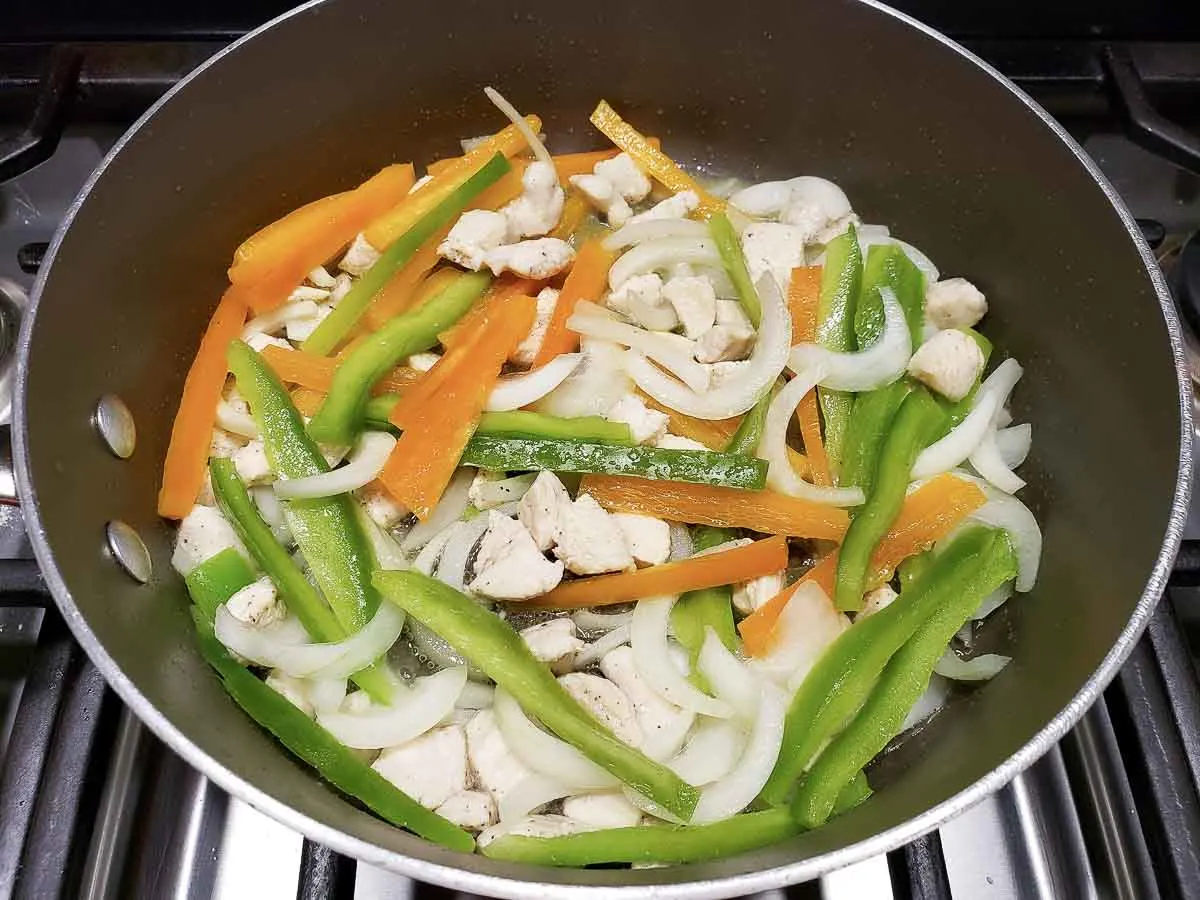sliced fajita veggies and chicken cooking in a pan.