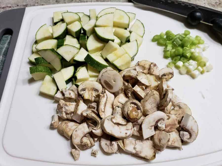 aboborinha picada, cogumelos e cebola verde num tabuleiro de corte branco