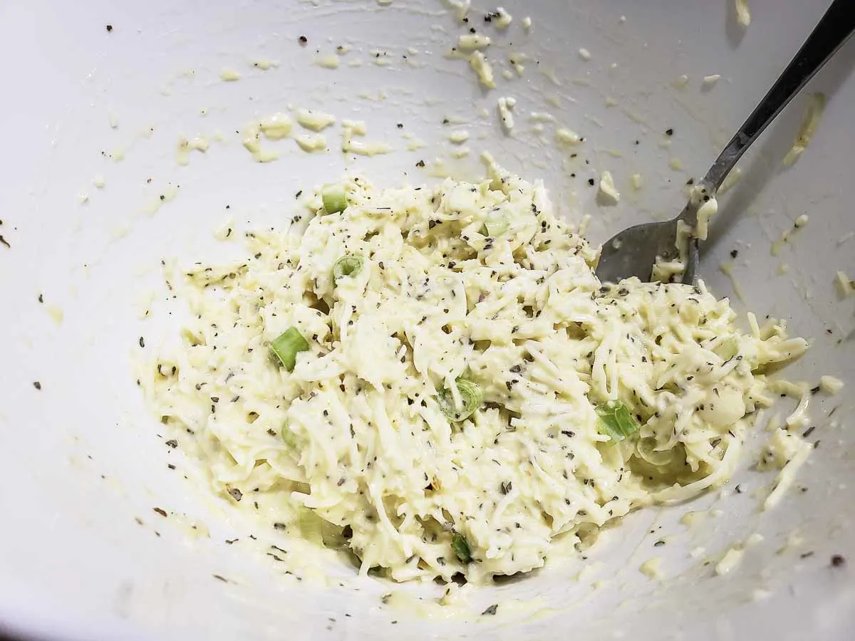 italian shredded cheese, sour cream, green onions, eggs, basil, salt, and pepper mixed in a bowl.
