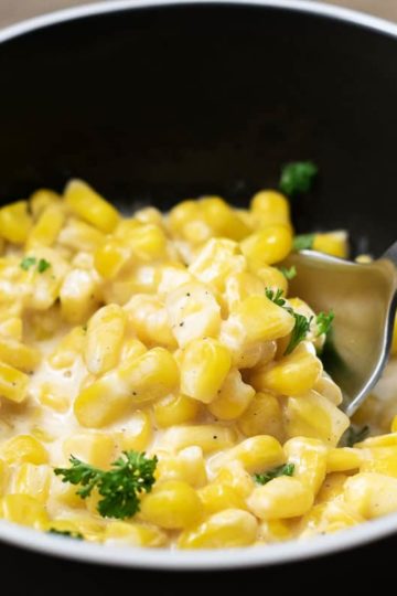 One Pot Cheesy Creamed Corn in a bowl with spoon lifting some corn