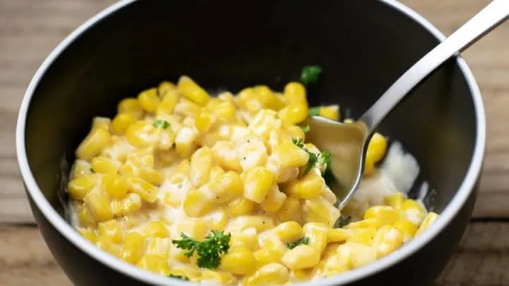 One Pot Cheesy Creamed Corn in a bowl with spoon lifting some corn