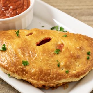 one Puff Pastry Pizza Calzone on a platter with a side of pizza sauce