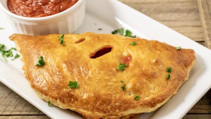 one Puff Pastry Pizza Calzone on a platter with a side of pizza sauce
