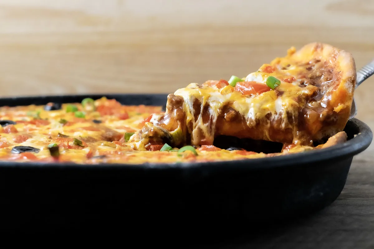 front view of Mexican pizza with a slice being lifted up.