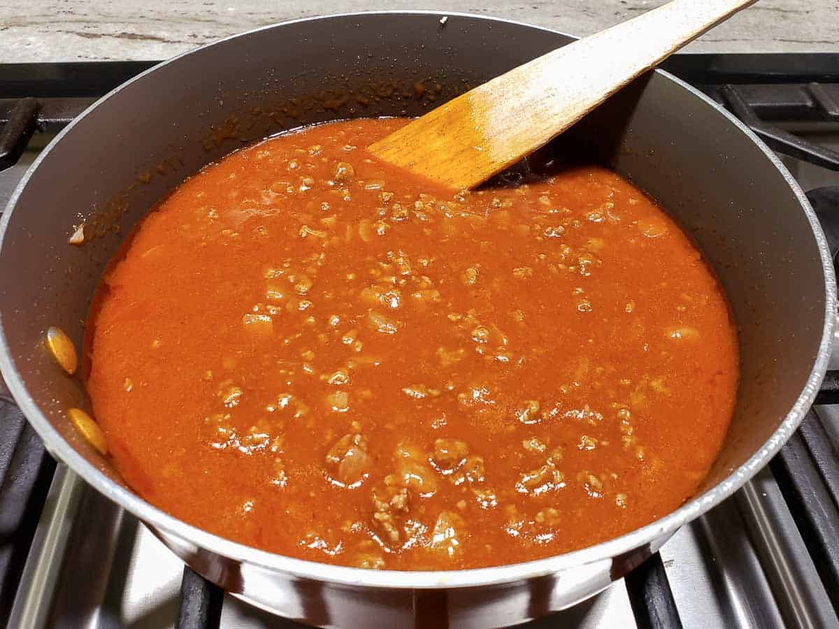 enchilada sauce mixed into ground beef cooking in a pan.