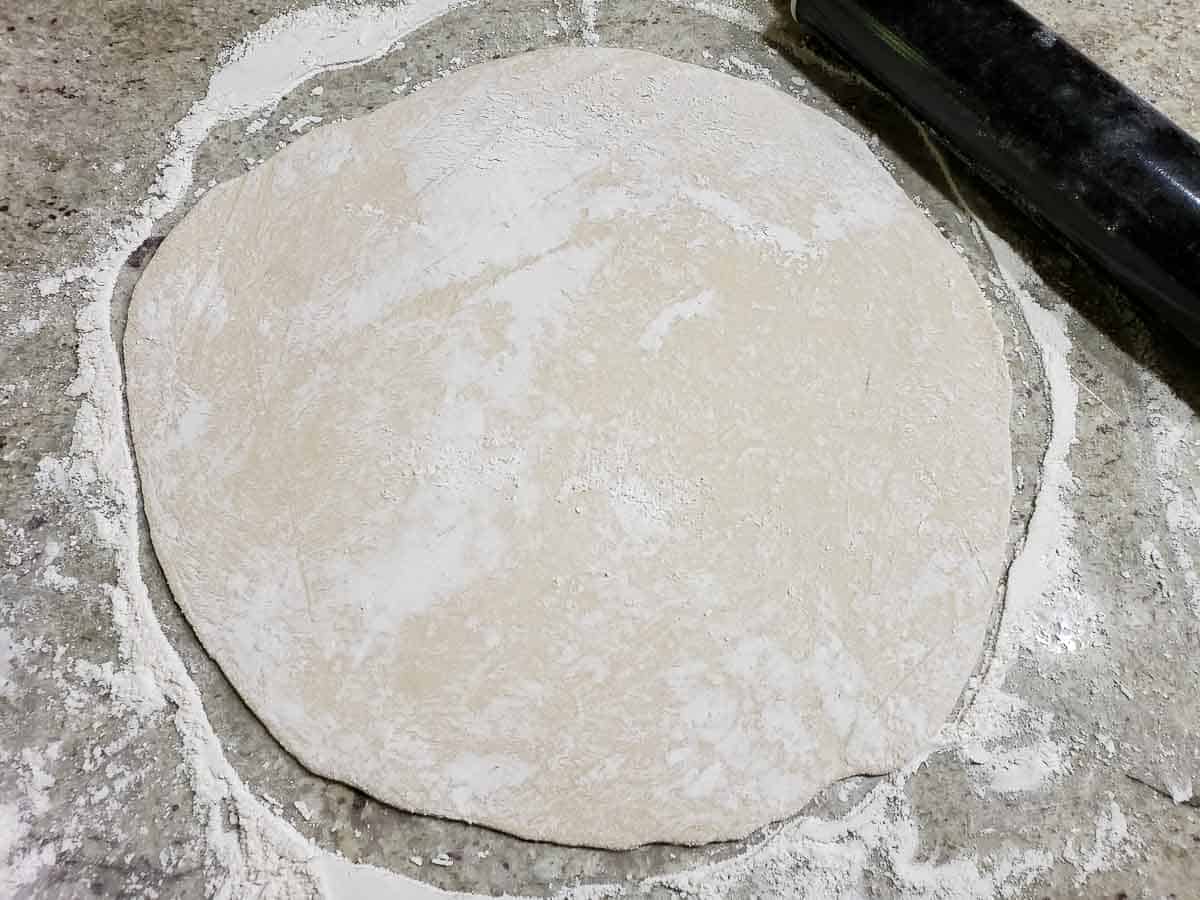 pizza dough rolled into a circle on a floured surface.