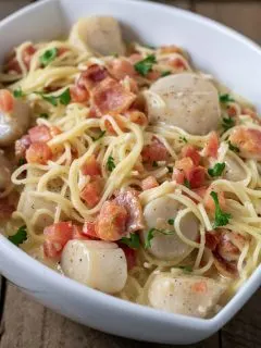 a close up front view of Cheesy Garlic Bacon Scallops and Linguine served in a white dish
