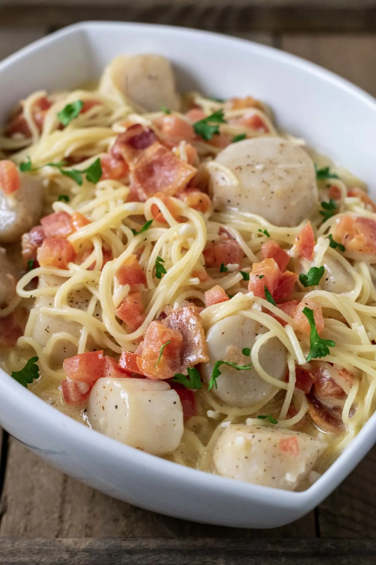 a close up front view of Cheesy Garlic Bacon Scallops and Linguine served in a white dish